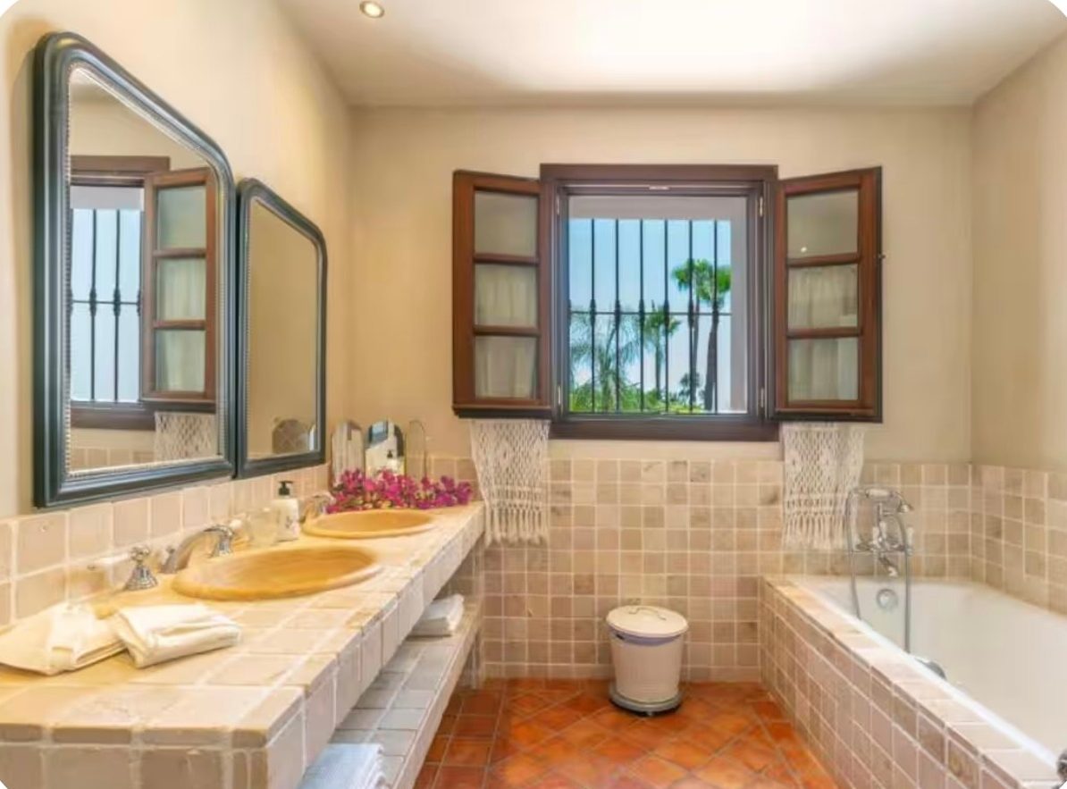 Stone-tiled bathroom with double basins, a bath and palm views